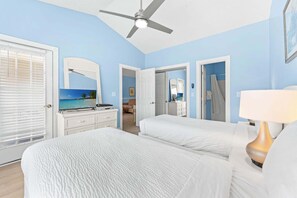 Une chambre d’hôtel avec un lit, une commode, un ventilateur de plafond et une salle de bain visible à travers une porte ouverte.