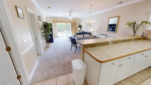 A spacious kitchen with a large island, a dining area with a black leather sofa, and a chandelier. - Escape to Nature | Pool & Golf Views | Magnolia Pointe 4877-104 (Myrtle Beach)