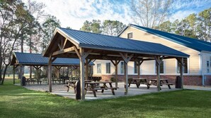 A covered picnic area with benches and tables, surrounded by a building with a blue roof and brick walls. - Escape to Nature | Pool & Golf Views | Magnolia Pointe 4877-104 (Myrtle Beach)