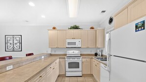 A modern kitchen with light wood cabinets, a white refrigerator, a microwave, and an oven. - Myrtlewood Resort Escape with Pool Access | Magnolia Pointe Luster Leaf 4883-203 (Myrtle Beach)