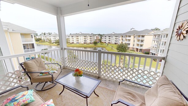 A balcony with a view of a residential area, a table with a vase of flowers, and two chairs.