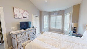 A bedroom with a bed, a dresser, a television, and a sign that says "LOVE Always Trusts".