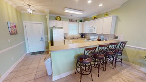 A kitchen with a central island, bar stools, a refrigerator, and a microwave.