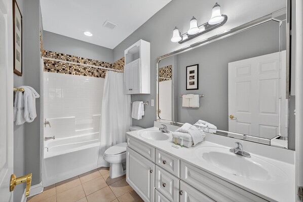 A modern bathroom with a bathtub, toilet, and double sink vanity.