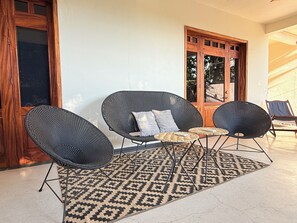 Une pièce avec un tapis à motifs, deux fauteuils en osier noirs, une petite table et une porte en bois.