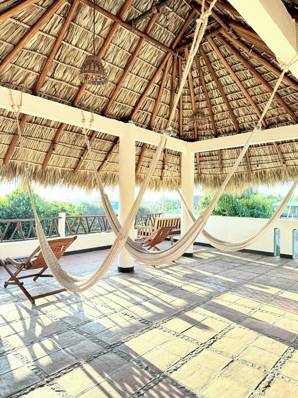 A covered outdoor area with a thatched roof, wooden furniture, and a hammock.