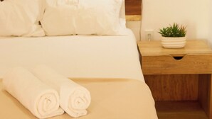 A neatly made bed with white linens, a wooden headboard, a bedside lamp, and a small potted plant on a wooden nightstand.