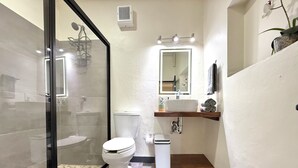 A bathroom with a glass shower enclosure, a toilet, a sink with a wooden countertop, and a mirror above the sink.