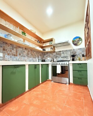 A kitchen with green cabinets, a stove, and a tiled backsplash.