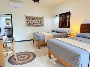 Habitación de hotel con dos camas, cabecera de madera, lámpara de noche, aire acondicionado de pared y un pequeño escritorio con silla.