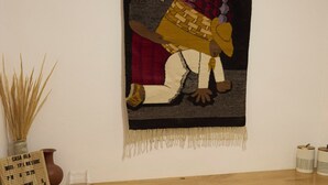 A bar area with a woven tapestry, a sign, and three stools.