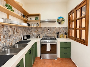 A kitchen with a gas stove, double sink, green cabinets, and a tiled backsplash.
