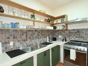 Una cocina con estufa a gas, dos fregaderos y una variedad de utensilios de cocina en estantes.