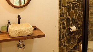 A bathroom with a stone wall, a wooden sink, a mirror, and a toilet.