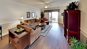 A spacious living room with a sofa set, a coffee table, and a red armchair. There is a wooden cabinet and a ceiling fan. - Magnolia Pointe Retreat Near the Beach | Magnolia Pointe Magnolia Lake 4812-201 (Myrtle Beach)