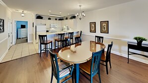 A dining area with a round table and chairs, a kitchen in the background, and a hallway leading to another room. - Magnolia Pointe Retreat Near the Beach | Magnolia Pointe Magnolia Lake 4812-201 (Myrtle Beach)