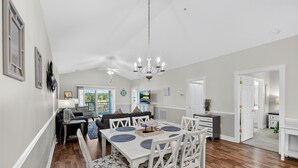 A spacious dining area with a white table and chairs, a chandelier, and a view of the kitchen in the background. - Bright and Inviting Magnolia Pointe Lakefront Condo | Magnolia Pointe Magnolia Lake 4828-402 (Myrtle Beach)