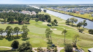 A golf course with a river, trees, and residential buildings in the background.