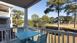 A covered outdoor area with a table and chairs, overlooking a golf course with trees and a clear sky.