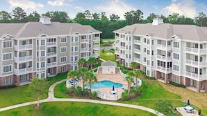 A multi-story hotel with a central courtyard featuring a swimming pool, surrounded by lounge chairs and palm trees.