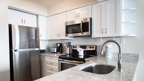 A modern kitchen with stainless steel appliances, white cabinets, and a granite countertop.