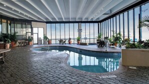An indoor swimming pool with a tiled floor, surrounded by potted plants and seating areas.