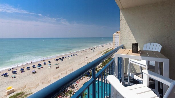 Un balcon avec vue sur une plage, une piscine et une table avec des chaises.