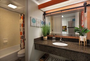 Une salle de bain avec un comptoir en granit, un lavabo blanc, un miroir et un rideau de douche à motifs géométriques.