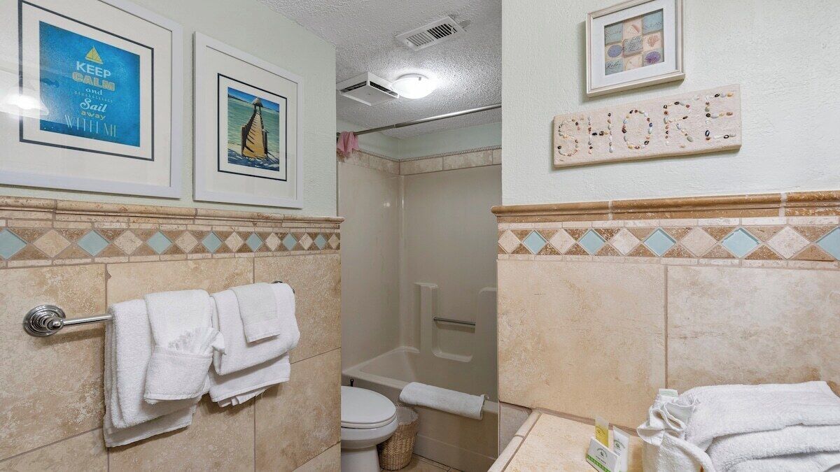 A bathroom with a shower, toilet, and towel rack. There are framed pictures on the wall and a sign that says "SHORE".