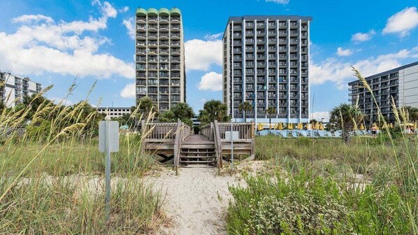 A pathway leading to a beach area with tall buildings in the background.