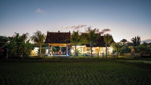 A traditional building with a tiled roof and a covered porch, surrounded by a well-maintained garden and a rice field.