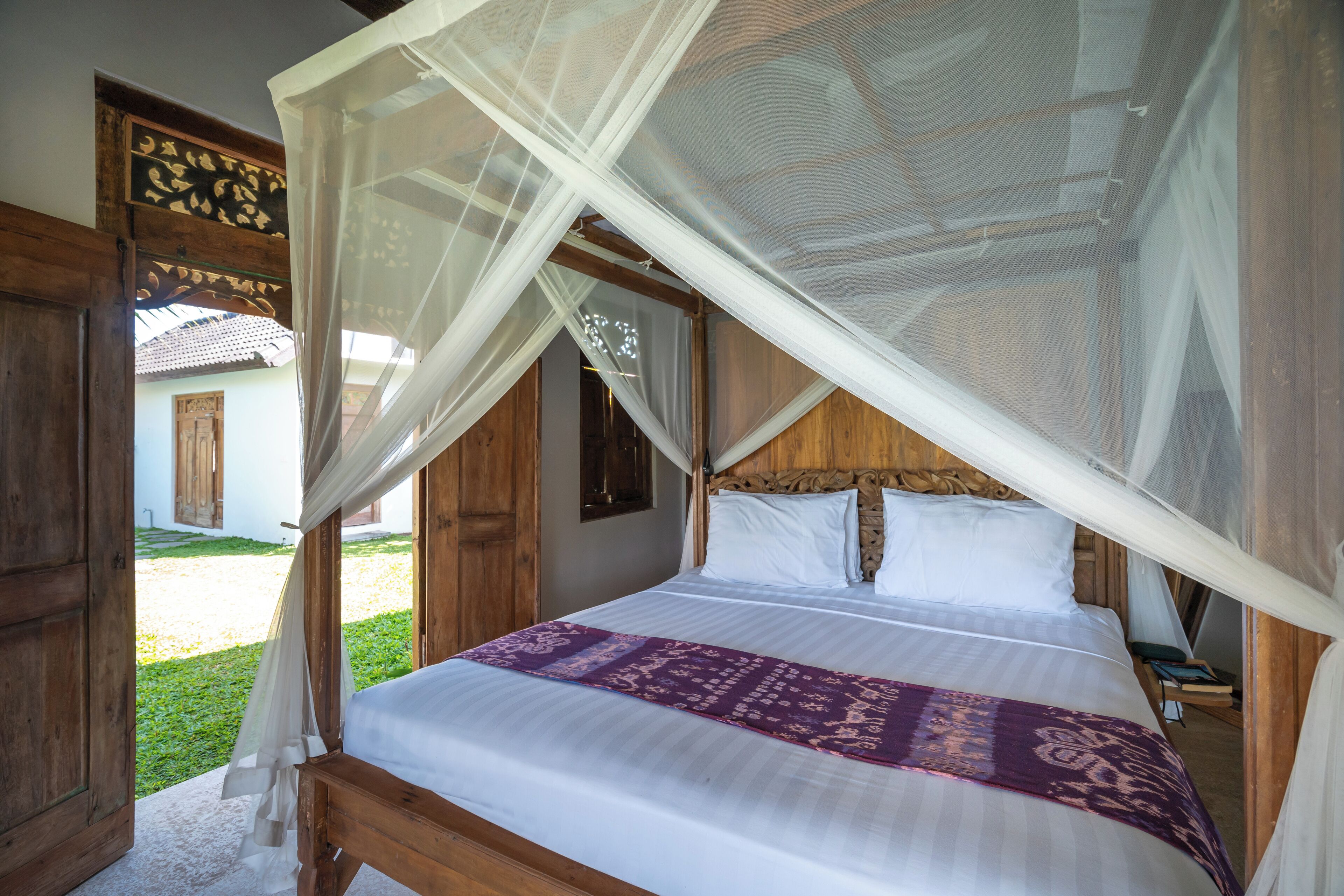 A bed with a canopy, wooden headboard, and a purple bedspread.