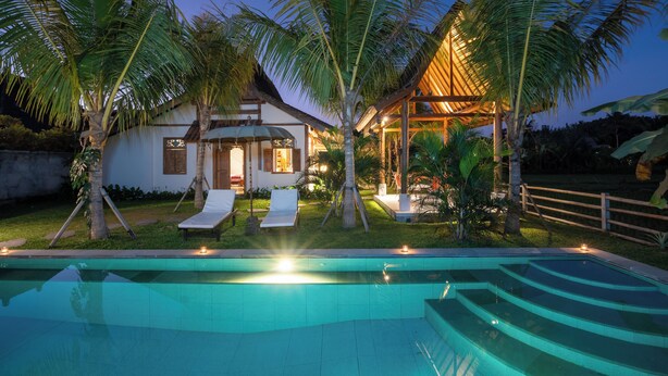 A poolside area with a house, palm trees, and a wooden deck.