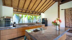 A modern kitchen with a large island, stainless steel appliances, and a view of lush greenery outside.