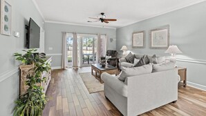 Ein Wohnzimmer mit grauem Sofa, einem Holztisch und einem Deckenventilator.