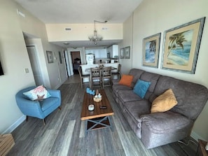 A living room with a gray sofa, a blue armchair, a wooden coffee table, and a dining area in the background.