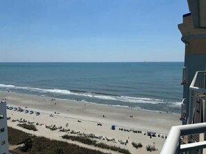 Blick auf einen Strand vom Balkon aus, mit blauem Himmel, Sandstrand und dem Meer.