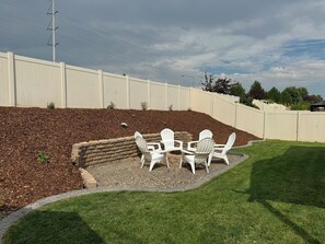 A backyard with a white fence, a stone fire pit, and white chairs. - Family-Friendly Stylish 5BR w/ Theater & Hot Tub in Meridian Idaho (Meridian)