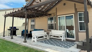 Un patio couvert agrémenté d’une pergola en bois, de meubles d’extérieur et d’un barbecue.
