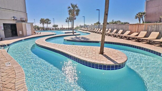 A pool area with a curved design, palm trees, and lounge chairs.