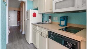 A compact kitchen with white cabinets, a microwave, a coffee maker, and a dishwasher.