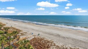 A beach with a wooden walkway leading to the shore, palm trees, and a clear blue sky. - Savoy 3BR Oceanfront Condo + Gym & Beach Access! | Savoy PH (Myrtle Beach)