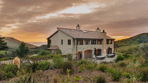 Une maison à deux étages avec une façade en pierre, un toit en tuiles et un patio aménagé avec du mobilier d’extérieur.