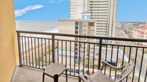 Un balcon avec vue sur la plage et un grand immeuble en arrière-plan.