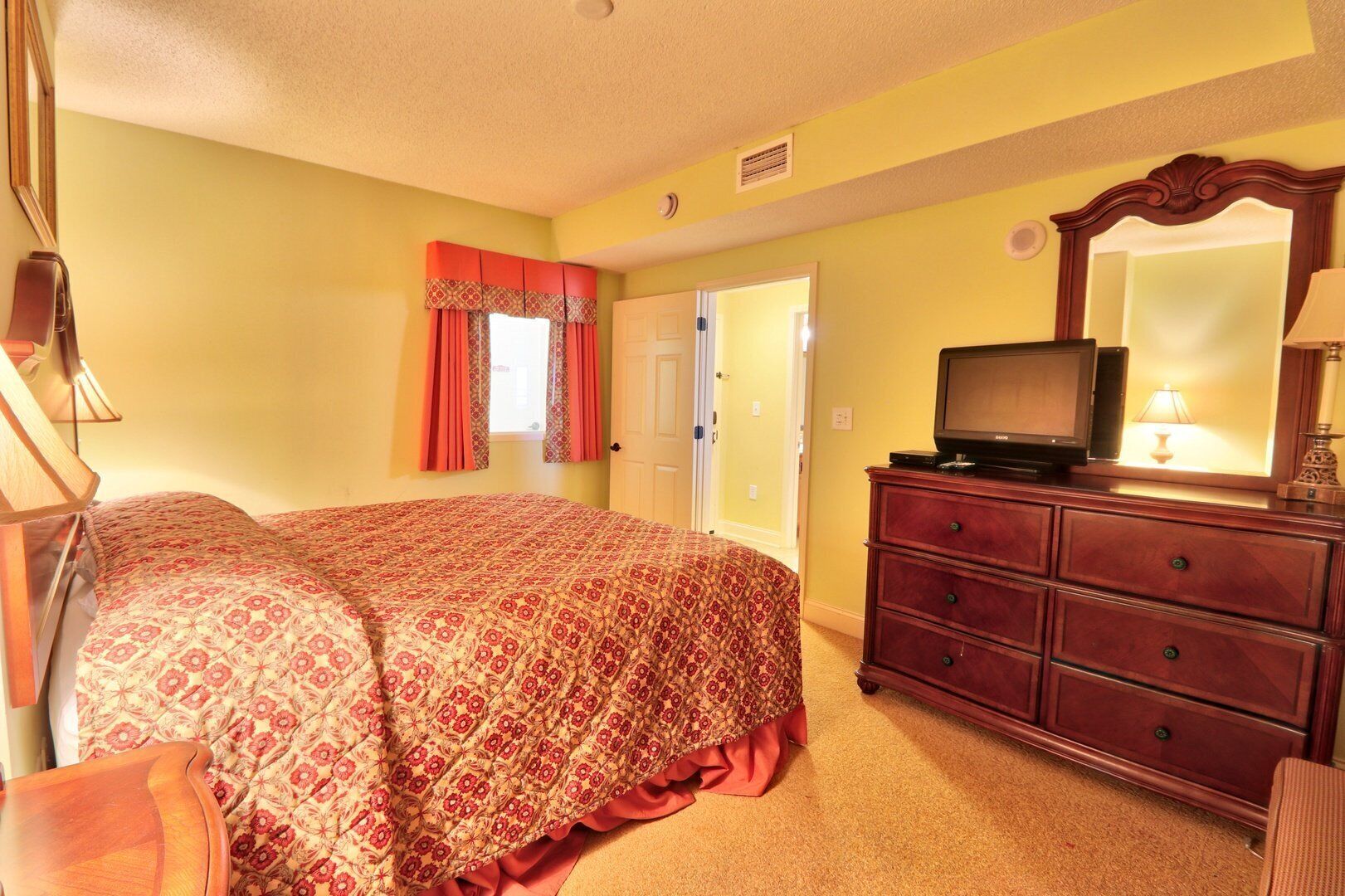 A bedroom with a bed, dresser, television, and a mirror.