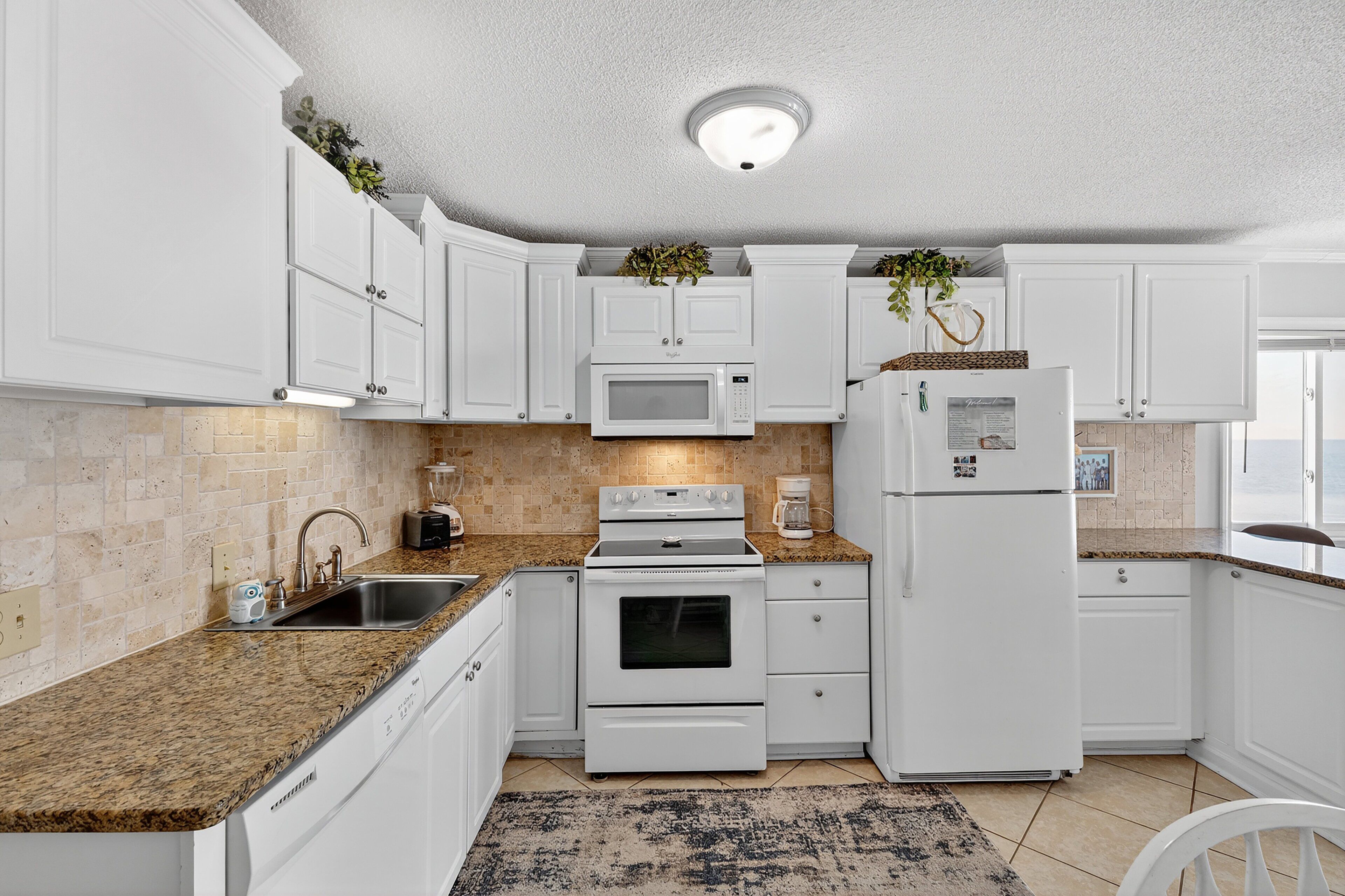 A kitchen with white cabinets, a granite countertop, a built-in microwave, an oven, a refrigerator, and a window providing natural light.