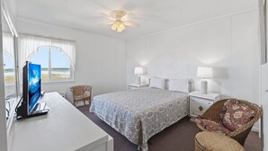 A hotel room with a bed, two bedside tables with lamps, a desk with a computer, a chair, and a ceiling fan. - Cozy Condo | Stunning Ocean View in Myrtle Beach | A Place at the Beach IV G231 (Myrtle Beach)
