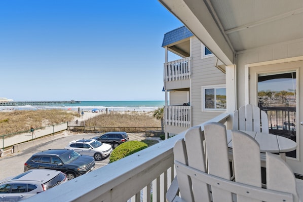 Un balcon avec vue sur la plage, les voitures garées et une jetée au loin.