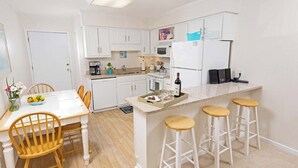 A modern kitchen with white cabinets, a central island with stools, a dining table with chairs, and a small bar area.
