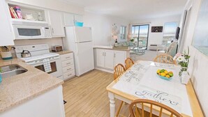 A modern kitchen with white cabinets, a microwave, stove, and a dining table set for four with a 'Gather' placemat.